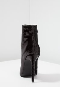 Černá kotníková bota s flitry, špičatou špičkou a jehlovým podpatkem, má hladkou strukturu a zapínání na zip vzadu.