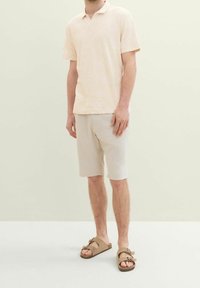 Ljusrosa kortärmad polotopp med ett subtilt bladmönster, samsytt med ljusbeiga shorts och bruna sandaler med en båtaccent.