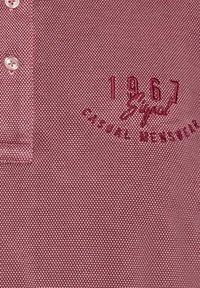 Koszula polo w teksturowanej bordowej tkaninie z trzema guzikami, wyhaftowanym napisem "1967" oraz "Casual Menswear" w ciemnoczerwonym kolorze.