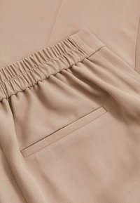 Beige kangas yenye uso wa muundo, ukanda wa elastiki uliojaa, na kidogo cha mfuko wa kushona.