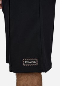 Shorts noirs en tissu texturé avec un logo "PEgADOR" brodé en rouge et blanc sur un badge rectangulaire près de l'ourlet.