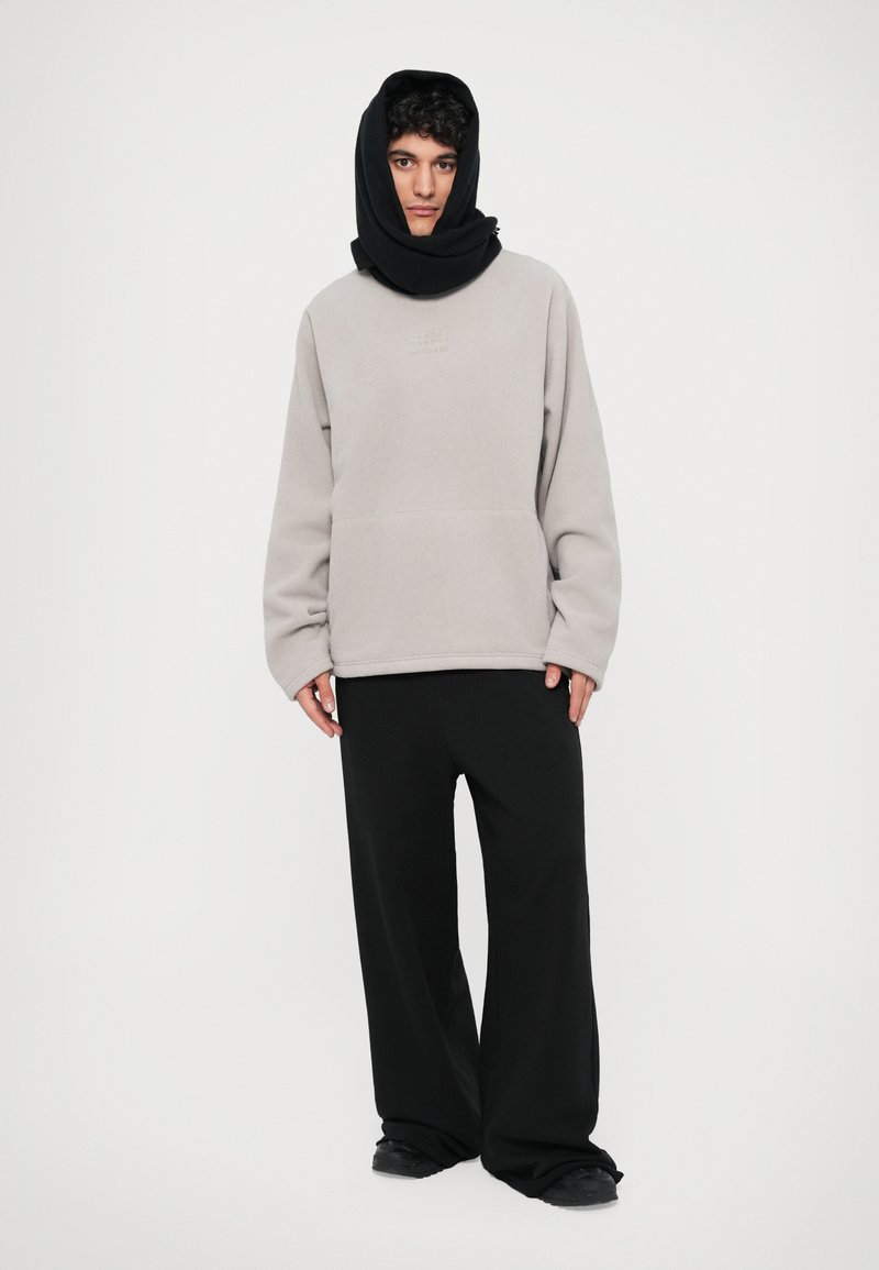 Gray fleece sweatshirt with a black hood, relaxed fit, featuring a front pocket. Paired with wide-leg black pants and dark footwear.