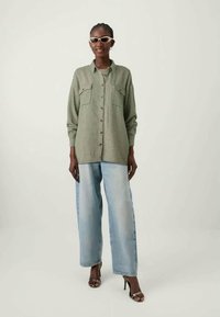 Green checked oversized shirt with two chest pockets, paired with light blue wide-leg jeans and transparent heeled sandals.