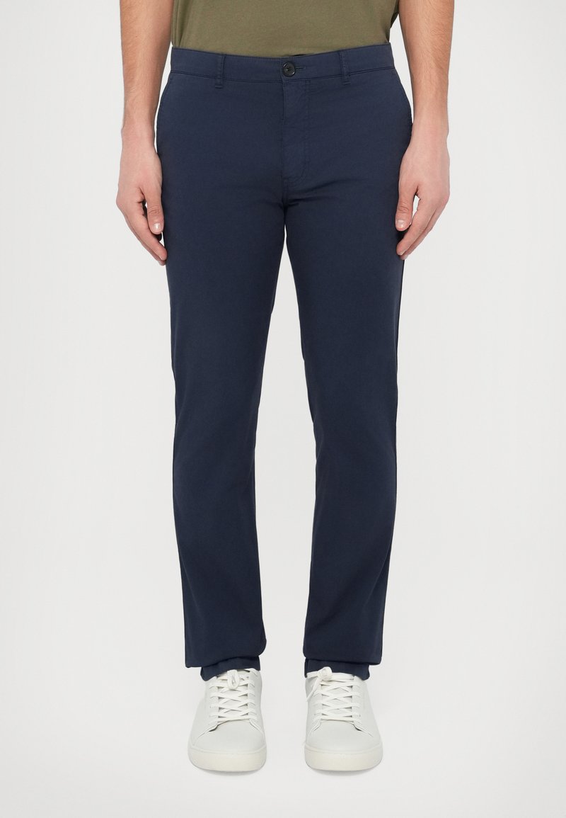 Tmavomodré chino nohavice z bavlnenej zmesi. Majú zapínanie na gombík a pútka na opasok. Kombinované s bielymi teniskami. Dizajn v úzkom strihu.
