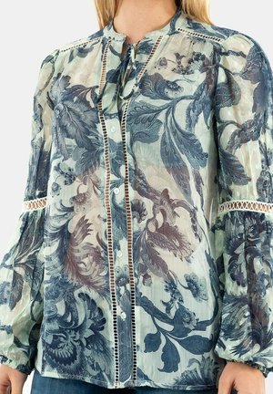 Blouse longue transparente à manches longues avec motifs floraux bleus et gris, boutonnée à l’avant, col à nouer et bordure en dentelle aux manches et sur la patte de boutonnage.