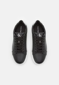 Czarne skórzane sneakersy z białymi gumowymi podeszwami. Cechy to sznurówki, wyściełany kołnierz oraz akcent logo na języku.