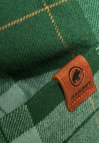 Zielona wełniana tkanina w kratkę o miękkiej fakturze; posiada brązową skórzaną metkę z wytłoczonym logo. Złote akcenty podkreślają wzór.