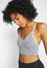 Crop top gris en tissu texturé avec un décolleté en V et des fines bretelles, présentant un motif chiné subtil et des finitions élastiques.