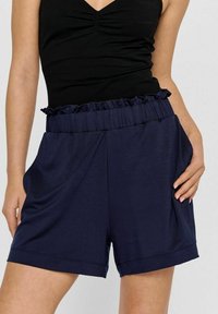 Marineblaue Shorts mit einem Rüschengummi-Bund, lockerer Passform, Seitentaschen und einer glatten Textur, die für Komfort und Vielseitigkeit entworfen wurden.