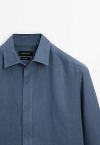 Blå linneskjorta med knapp-ned krage, synliga sömmar och en texturerad väv. Har fem knappar längs framplacket.