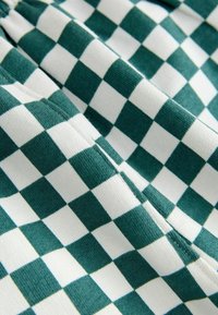 Zeleno-bielo károvaná látka s hladkou textúrou a striedavými štvorcami; švy sú viditeľné pozdĺž okrajov.