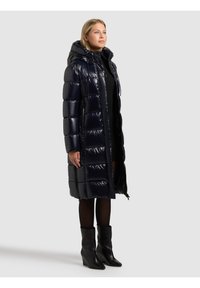 Tumši zila pūtuma jaka ar spīdīgu virsmu, kapuci un rāvējslēdzēja aizdari. Raksturīgas vertikālas dūriena joslas un sānu kabatas. Valkāta kopā ar melnu apģērbu un zābakiem.