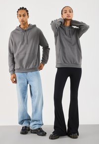 Due persone che indossano felpe grigie; una con jeans azzurri chiari e sneakers nere, l'altra con pantaloni neri a palazzo e stivali neri.