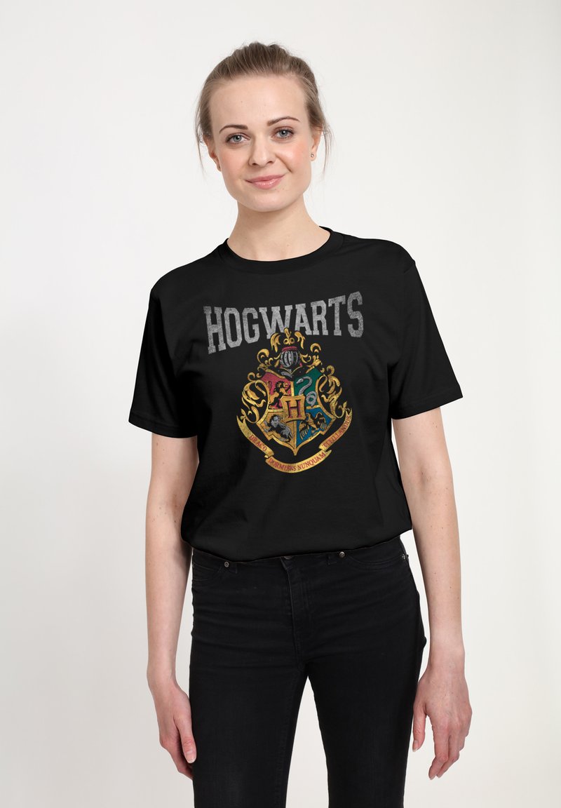 Czarna bawełniana koszulka z dużym herbem Hogwartu w złotych i kolorowych akcentach, z napisem "HOGWARTS" powyżej w szarym kolorze.