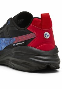 Fekete és piros sportcipő, texturált sarokkal, kék kockás mintával és BMW Motorsport márkajelzéssel. Jellemzője egy kiemelkedő húzószíj és tartós talp.