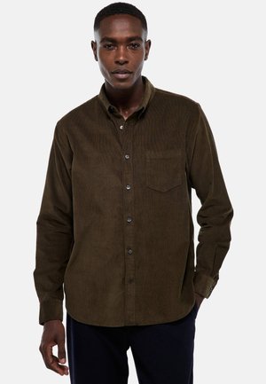 Chemise en velours côtelé marron avec un col boutonnière, des manches longues et une poche poitrine simple. Présente un tissu texturé et des boutons noirs.