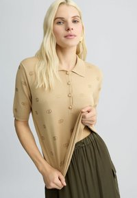 Beige polo shirt met korte mouwen, voorzien van een subtiel stippenpatroon, drie knopen bij de kraag en een zachte, gebreide textuur.