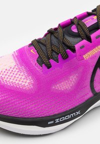 Gros plan d'une chaussure de course Nike ZoomX violet vif avec des lacets noirs et jaunes et des détails noirs sur la semelle.