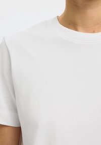 Gros plan d'une personne portant un t-shirt blanc uni à col rond montrant la partie supérieure de la poitrine et du cou.