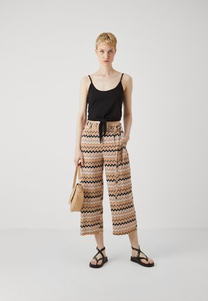 Black tank top with a tie front, paired with patterned wide-leg pants in orange, cream, and black zigzag design. Includes a beige handbag and black sandals.