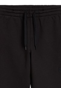 Zwarte joggingsbroek van zacht materiaal met een elastische tailleband, trekkoord en een klein logopatch aan de voorkant.