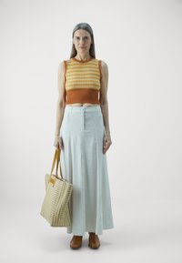 Top court en tricot orange et jaune, jupe maxi bleu clair, chaussures à lacets marron et sac en osier à rayures.