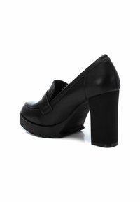 Zapato de tacón alto de cuero negro con punta redonda, plataforma gruesa y suela texturizada. El diseño cuenta con una correa decorativa en la parte superior.