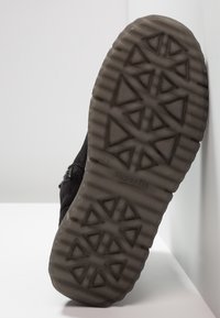 Podešev černé boty s trojúhelníkovým a vroubkovaným vzorem, na bílé ploše s názvem značky "superfit" a velikostí "31".