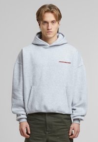 Grå hettegenser med lomme foran. Har "FORBUDT" i rød broderi på venstre bryst. Myk tekstur, avslappet passform.