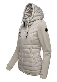 Beige puffer-jakke med hætte, lynlåslukning foran og to lynlåslommer. Blødt stof på ærmerne, tekstureret syning og logo på skulderen.