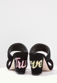 Černé semišové sandály na vysokém podpatku s vystřiženým designem, s vyšívanými nápisy "True" a "Love" na podpatcích v živých barvách.