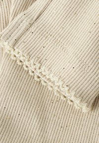 Beige ribstof met gouden spikkels, met een geschulpte gebreide rand langs de rand. Gevoerd en zacht met zichtbare stiksels.