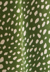 Zelená látka se vzorem malých, nepravidelných bílých teček. Textura se zdá být hladká a tkanina je hustá, bez viditelných ozdob.