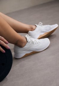 Λευκά αθλητικά παπούτσια με πλέγμα με υφή και λαστιχένια σόλα. Διαθέτουν χαμηλό προφίλ και κορδόνια, με καφέ λεπτομέρεια στη φτέρνα.