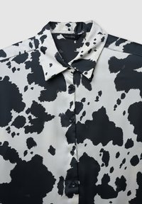 Blusa a righe bianche e nere con colletto, chiusura a bottoni e texture liscia simile alla seta. Presenta grandi macchie irregolari.