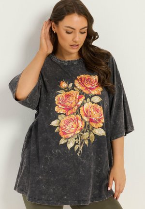 Woman with long brown hair wearing oversized faded black t-shirt with large orange rose graphic, touching hair and looking down.