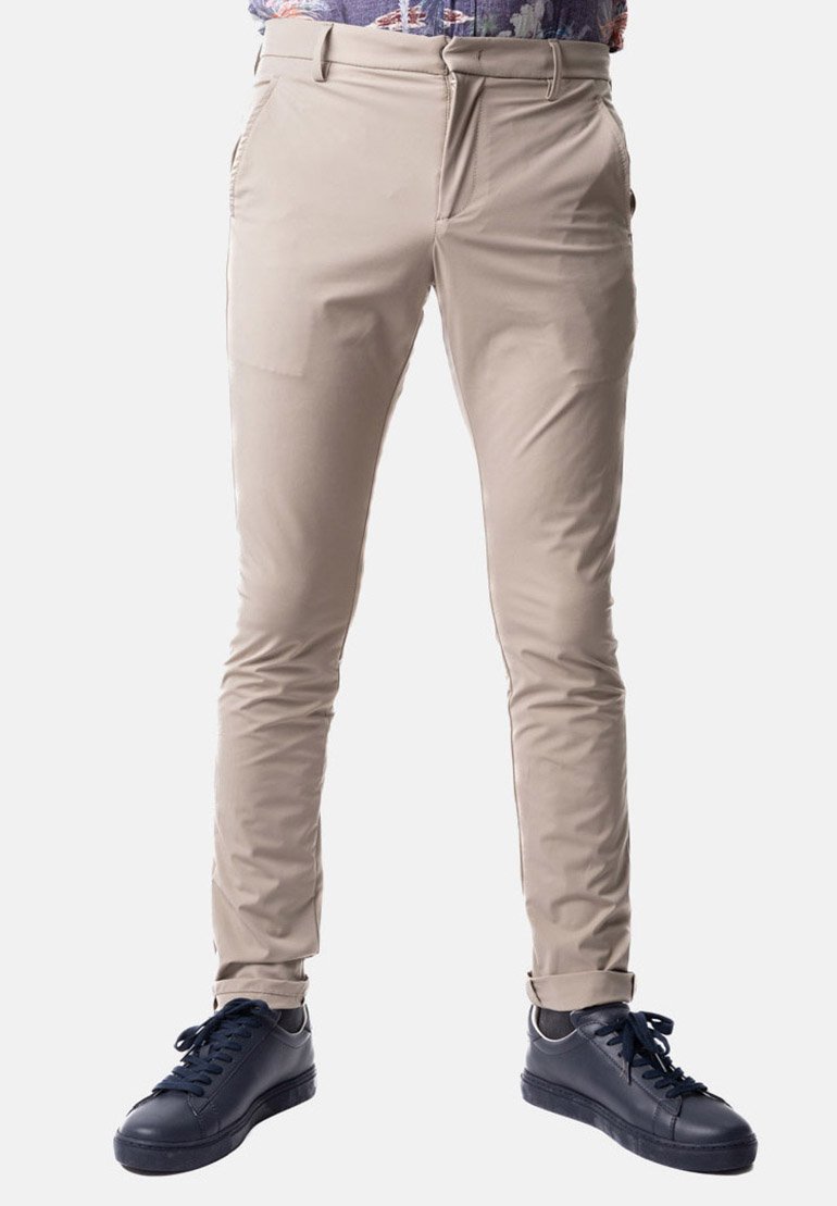 Pantaloni beige slim-fit realizzati in tessuto elasticizzato, con tasche laterali e una texture liscia, abbinati a sneaker scure.