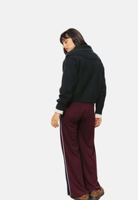Pull noir court avec un large col, associé à un pantalon large bordeaux aux accents rayés blancs. Chaussures à imprimé léopard.
