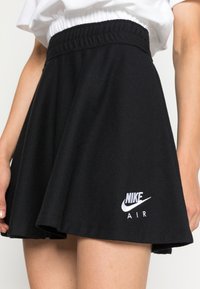 Svart skaterkjol i texturerad tyg, med resår i midjan och en broderad vit Nike Air-logga vid fållen.