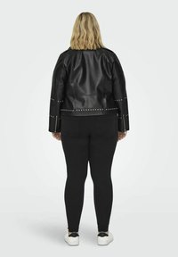 Svart konstläderjacka med nitar, boxig passform och långa ärmar. Matchad med svarta leggings och vita sneakers.