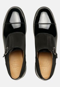 Schwarze Lederschuhe mit glattem Lackzehen, Wildlederoberteil und seitlichem Schnallendetail. Das Innere ist mit beigem Futter und geprägtem Markennamen ausgestattet.