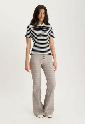 Jeune femme debout portant un polo à manches courtes rayé noir et blanc et un pantalon évasé beige à carreaux avec des détails de boutons.