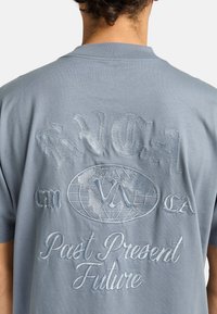 Lichtblauwe katoenen t-shirt met geborduurde tekst en een wereldbol ontwerp op de achterkant. Zachte textuur en een ontspannen pasvorm, met korte mouwen.