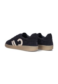 Navy blauw suède sneakers met een beige embleem en accenten, voorzien van een gestructureerde rubberen zool en een klassieke vetersluiting.