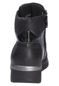 Bottine noire à finition brillante, partie supérieure en maille, fermeture éclair sur le côté, talon rembourré et accent argenté sur la semelle. Panneau arrière texturé.