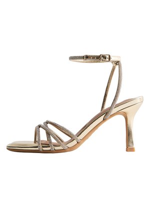 Gouden sandalen met hoge hak en dunne bandjes met strassstenen over de tenen, voorzien van een enkelriempje met gesp.
