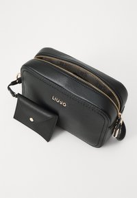 Schwarze Leder-Umhängetasche mit goldfarbener Reißverschluss, LIUJO-Logo und passendem kleinen Kartenetui. Glatte Textur, rechteckige Form, minimalistisches Design.