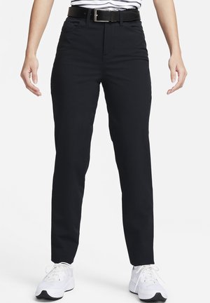 Persona con pantalones negros ajustados, zapatillas blancas, cinturón negro y camisa a rayas blancas y negras metida dentro.