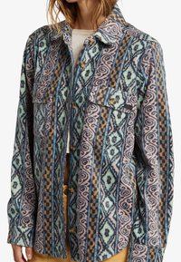 Fleece shirt with a multi-colored geometric pattern in blue, pink, and brown. Features two chest pockets and button closures.