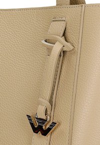 Beżowa skórzana torebka o teksturowej powierzchni. Posiada zaplanowaną rączkę oraz akcent z logo w odcieniu złotym. Widoczne detale przeszycia.
